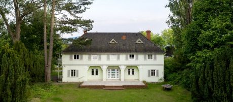 Großes  Haus mit mintfarbener Holzvertäfelung und hellgrauen Fensterläden und einer Veranda | Sparkasse Hannover