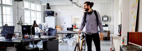 Junger Mann schiebt Fahrrad durchs Office | Sparkasse Hannover