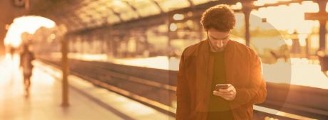 Junger Mann steht mit Handy am Bahngleis | Sparkasse Hannover
