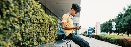 Junger Mann sitzt auf einer Mauer und schaut auf sein Smartphone | Sparkasse Hannover